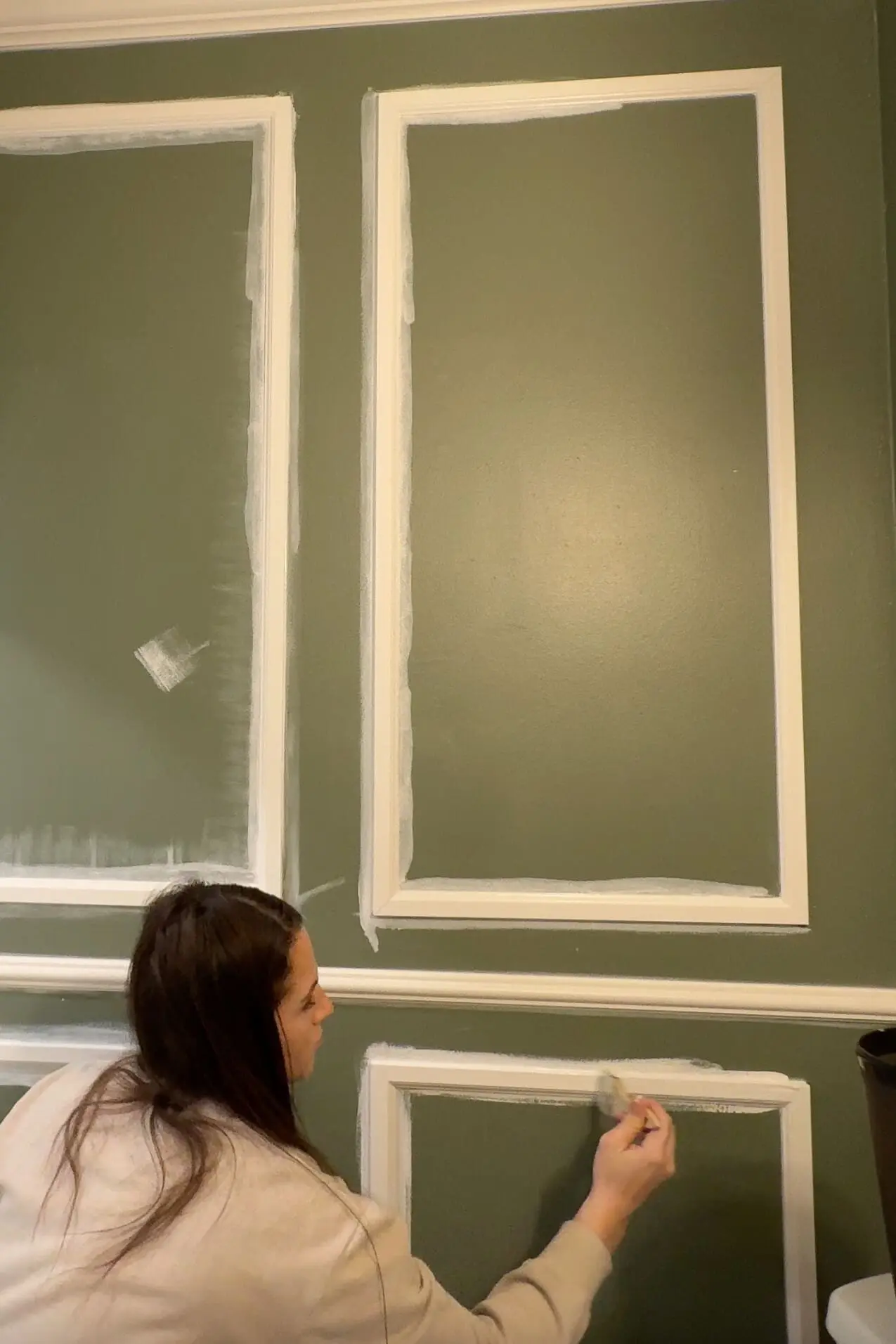 DIY enthusiast painting the white trim on a green wall with a brush, focusing on the intricate details of the trim accent wall design.